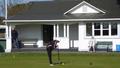 Photo of a person playing croquet outside of the Croquet Club, there is one person sitting on a bench watching and another person standing