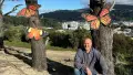 Artist Paul Forrest kneels in front of two trees with large butterfly sculptures attached to the trunks.