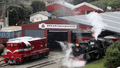 Red diesel locomotive and black steam locomotive emerging from a red storage building