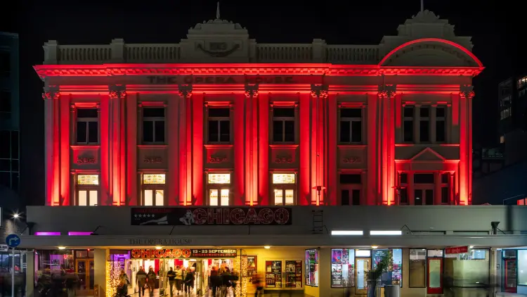 Nighttime photograph of the front of the Wellington Opera House, red lights illuminate the decorative columns.
