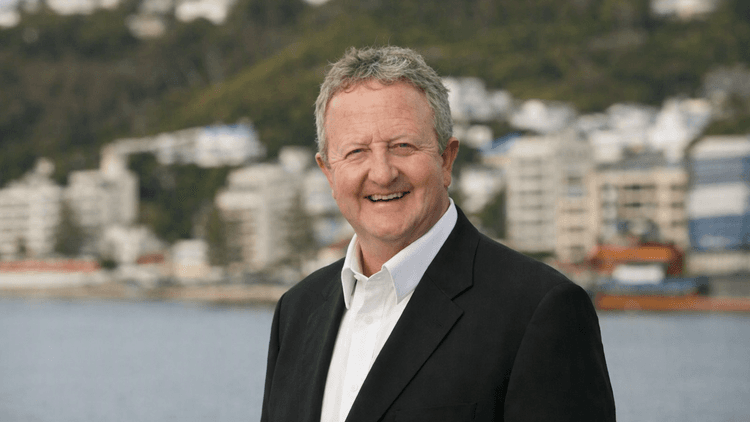 Man standing in front of Wellington harbour, smiling