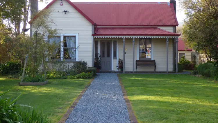 Photograph of a house with a red roof with a garden path and green lawns.