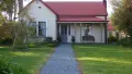 Photograph of a house with a red roof with a garden path and green lawns.