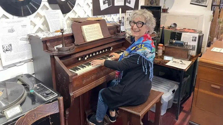 Woman smiling at camera, sitting at an old piano, groove disc records on wall