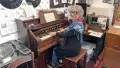 Woman smiling at camera, sitting at an old piano, groove disc records on wall