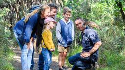 A family talks to a crouching man with a kea on his shoulder