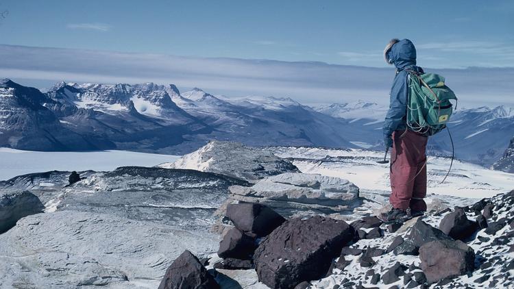 Lone figure to the right starring out at an expanse of snow covered mountains.