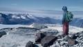 Lone figure to the right starring out at an expanse of snow covered mountains.