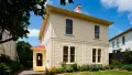 Photograph of Katherine Mansfield House, a cream coloured two-story square wooden building with a small flower garden out front, sunny