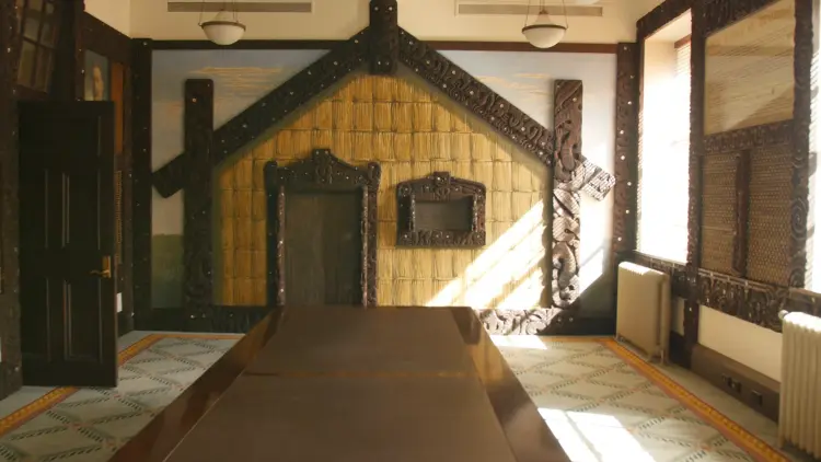 Interior shot of a side lit room with a facade of a Māori whare at the end of a table