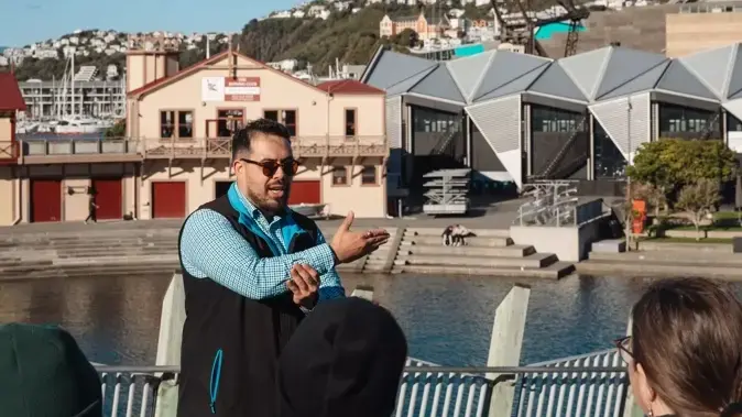 Man presenting to a group in front of lagoon and buildings
