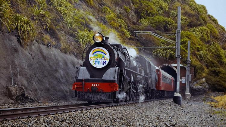 A black steam locomotive pulls carriages along a rain line and out a tunnel.