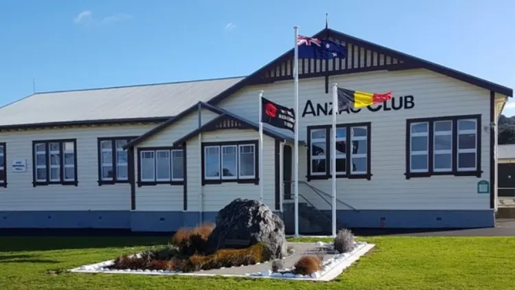 Building with dark coloured roof and three flags on flag poles in front, green lawn