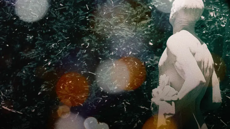 An artistic photograph. A marble statue stands on the right side, facing away from the camera. Bokeh light orbs obscure the view.