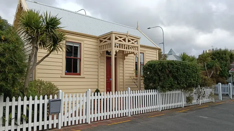 Yellow painted and white roof house behind a white picket fence