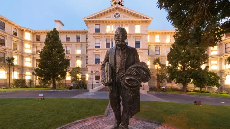Statue of politician in front of four storey white timber building
