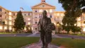 Statue of politician in front of four storey white timber building