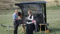 Two people stand next to a small trailer reading "Wet Plate Photographs" in vintage font.