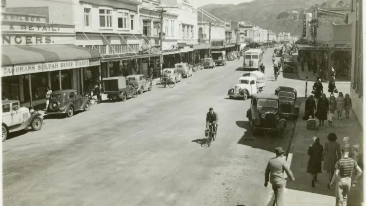 Sepia photograph of a street with parked cars, pedestrians and people riding bicycles