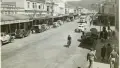 Sepia photograph of a street with parked cars, pedestrians and people riding bicycles
