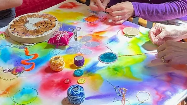 Photograph of a colourful table of arts and crafts with hands in action.