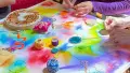 Photograph of a colourful table of arts and crafts with hands in action.