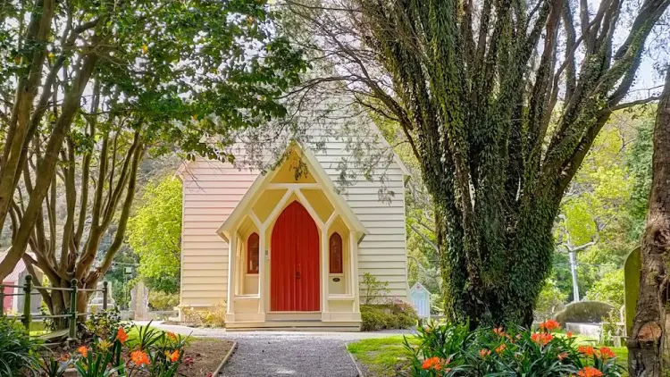 A photo of the path leading to the front of Christ Church, lined with orange flowers and shaded by trees.
