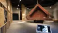 Inside a museum, a beautifully carved Māori pātaka stands surrounded by interpretation signs.