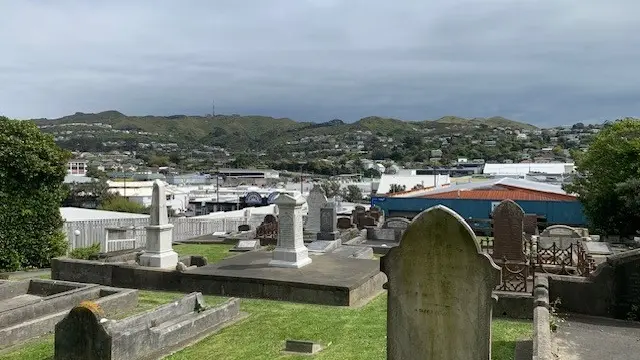 View of graveyard of green lawn and tombstones, city in the background and grey skies