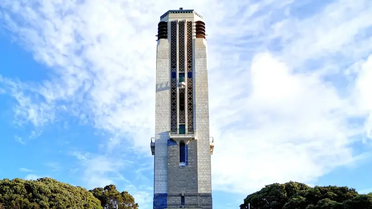 A photo of the Carillion in central Wellington, a tall grey brick tower against a cloud whipped blue sky.