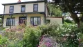 Colour photograph of the Half Way house, a yellow house surrounded by colourful flowers and garden
