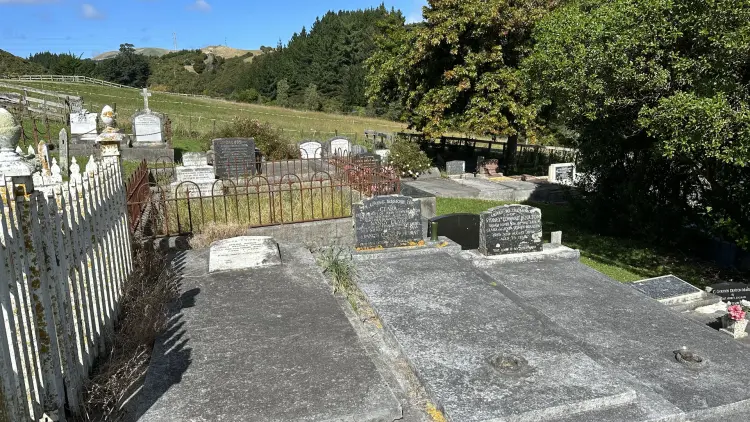 Graveyard with white picket fence on left and green trees on the right