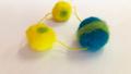 Photo of 2 yellow with green accents felted beads and one blue felted bead with a green accent connected by yellow string. 