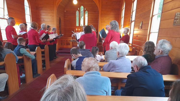 Interior shot of a wooden church. Singers in red perform in front of a seated audience.