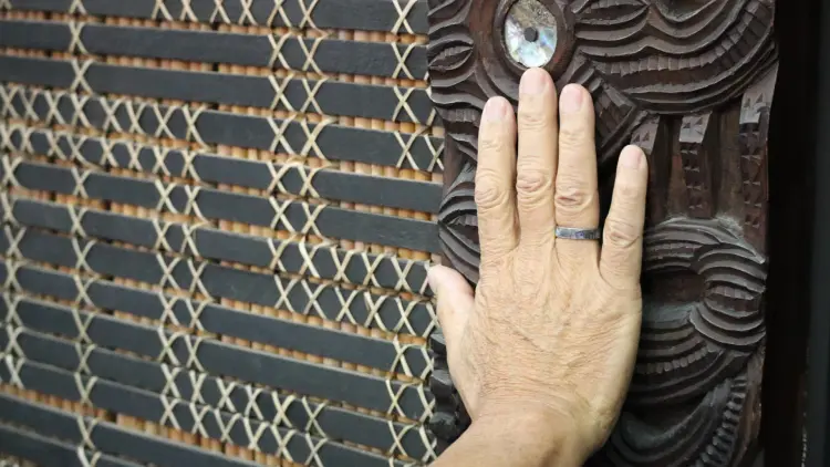 Close shot of a hand with a ring touching a carved panel with Māori designs