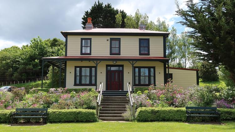 Colour photograph of the Half Way house, a yellow house surrounded by colourful flowers and garden