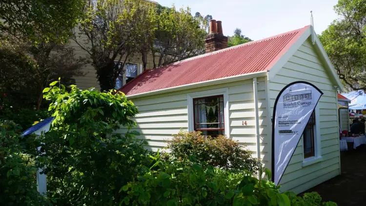 Yellow colonial building with red roof, white banner flag outside and green foliage