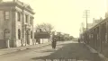 Sepia toned historic photo of a woman and child walking down Ōtaki Main Street 1923. Text at bottom reads "Mill Road Otaki NZ ©A7207"