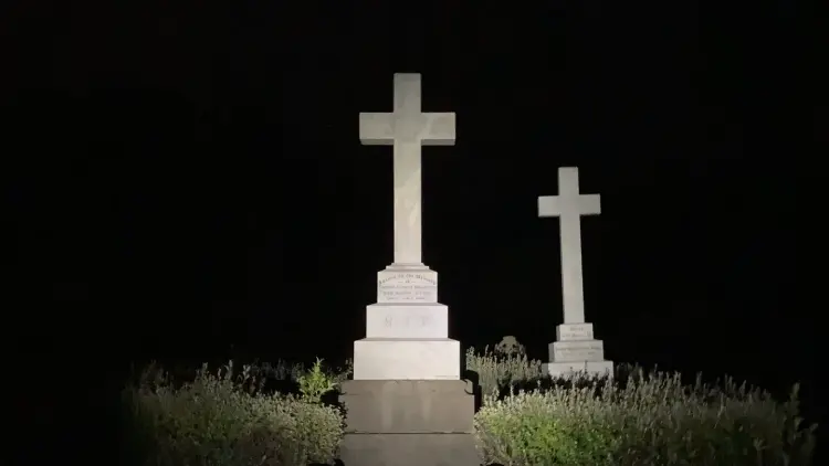A cemetery at night. Two white marble crosses stand out against the darkness illuminated by the flash of a camera.