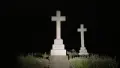 A cemetery at night. Two white marble crosses stand out against the darkness illuminated by the flash of a camera.