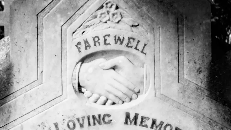 Black and white tombstone with text and engraving of clasped hands