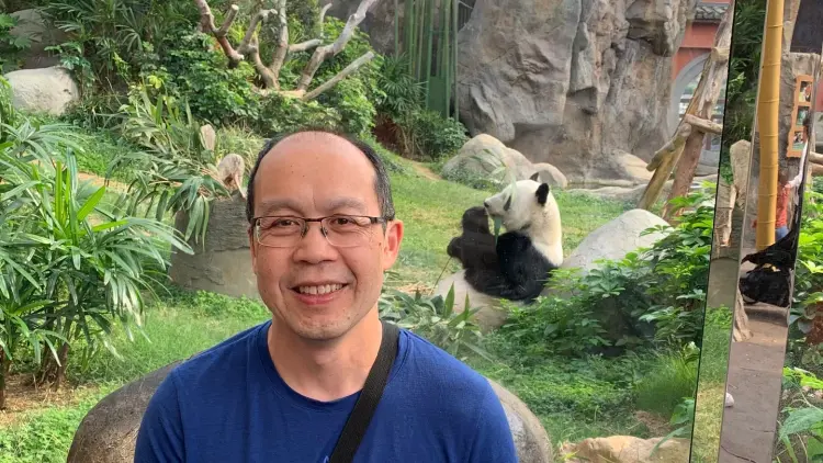 Man in blue shirt standing in front of giant panda enclosure