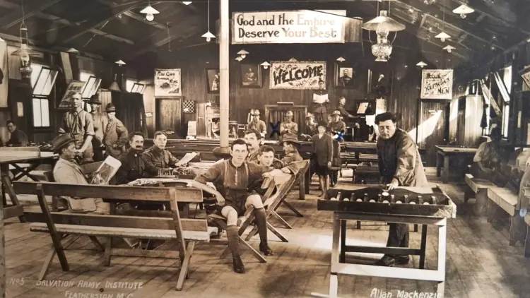 Historic sepia toned photo of the Anzac Hall interior, men sit on benches reading and playing games