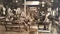 Historic sepia toned photo of the Anzac Hall interior, men sit on benches reading and playing games