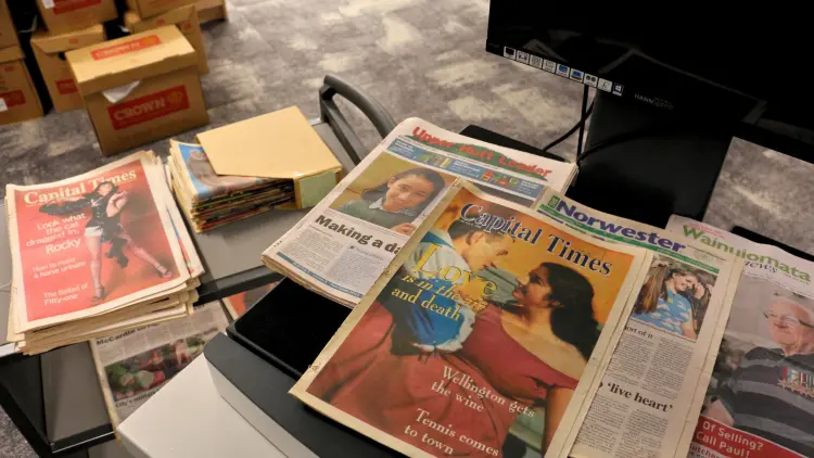 Photograph of a small table and library trolly with various old newspapers spread across them.