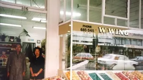 Photograph of a grocers and two people standing in the doorway