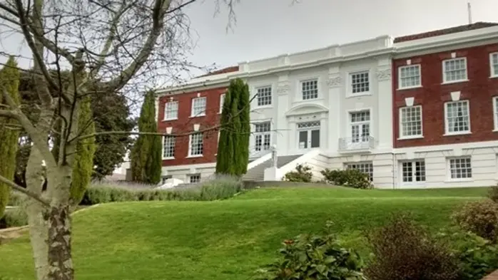 White and brown brick building with green lawn and trees outside