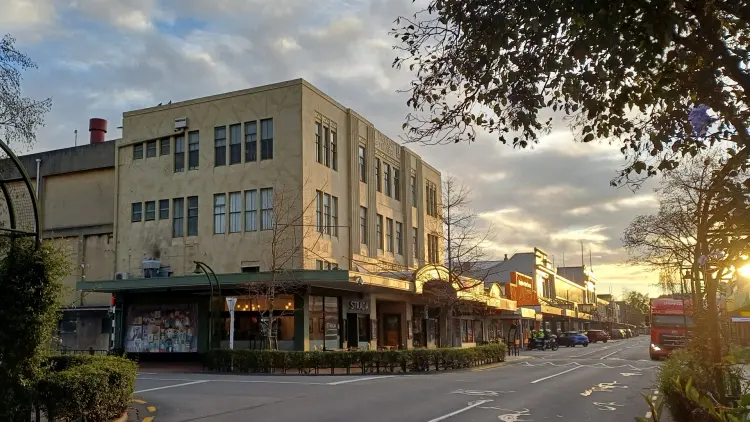 Colour photograph of a street with a yellow and beige building and shops