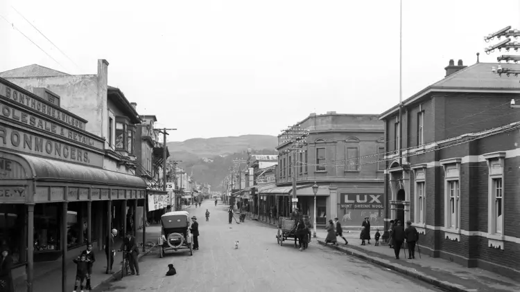 Black and white vintage photo of a street with cars and people.