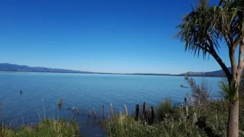 A view of a lake, blue skies, with a fence disappearing into the water.